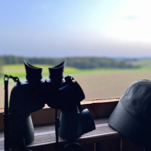 Ein Fernglas und eine Schirmmütze in einem Hochsitz vor dem Fenster